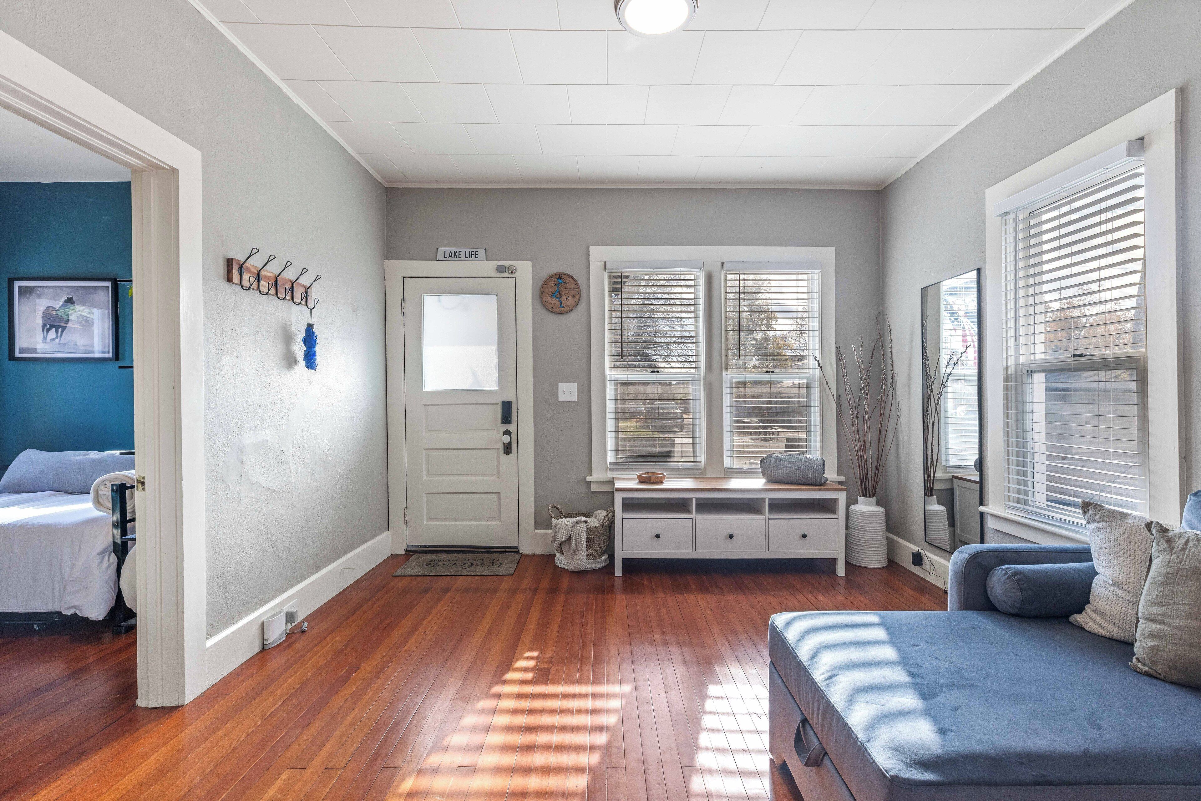A living room with hardwood flooring, a blue sofa, a white bench, and a door labeled "LAKE LIFE".