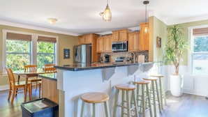 Una cocina moderna con armarios de madera, un refrigerador de acero inoxidable, un microondas y una isla grande con taburetes de bar.