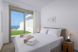 Ein Hotelzimmer mit einem großen Bett, einem Nachttisch mit Lampe und Blick auf das Meer durch eine Schiebetür.