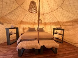 Una habitación tipo tienda de campaña, con cama, dos mesitas de noche y una lámpara colgante.