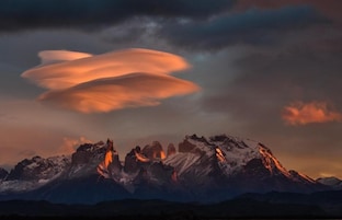 A mountain range with snow-covered peaks and a sunset sky.
