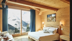 A wooden cabin bedroom with a bed, bedside tables, a window with curtains, and a view of mountains. - Chalet Morel 1586 - Hotel & Spa (Limone Piemonte)