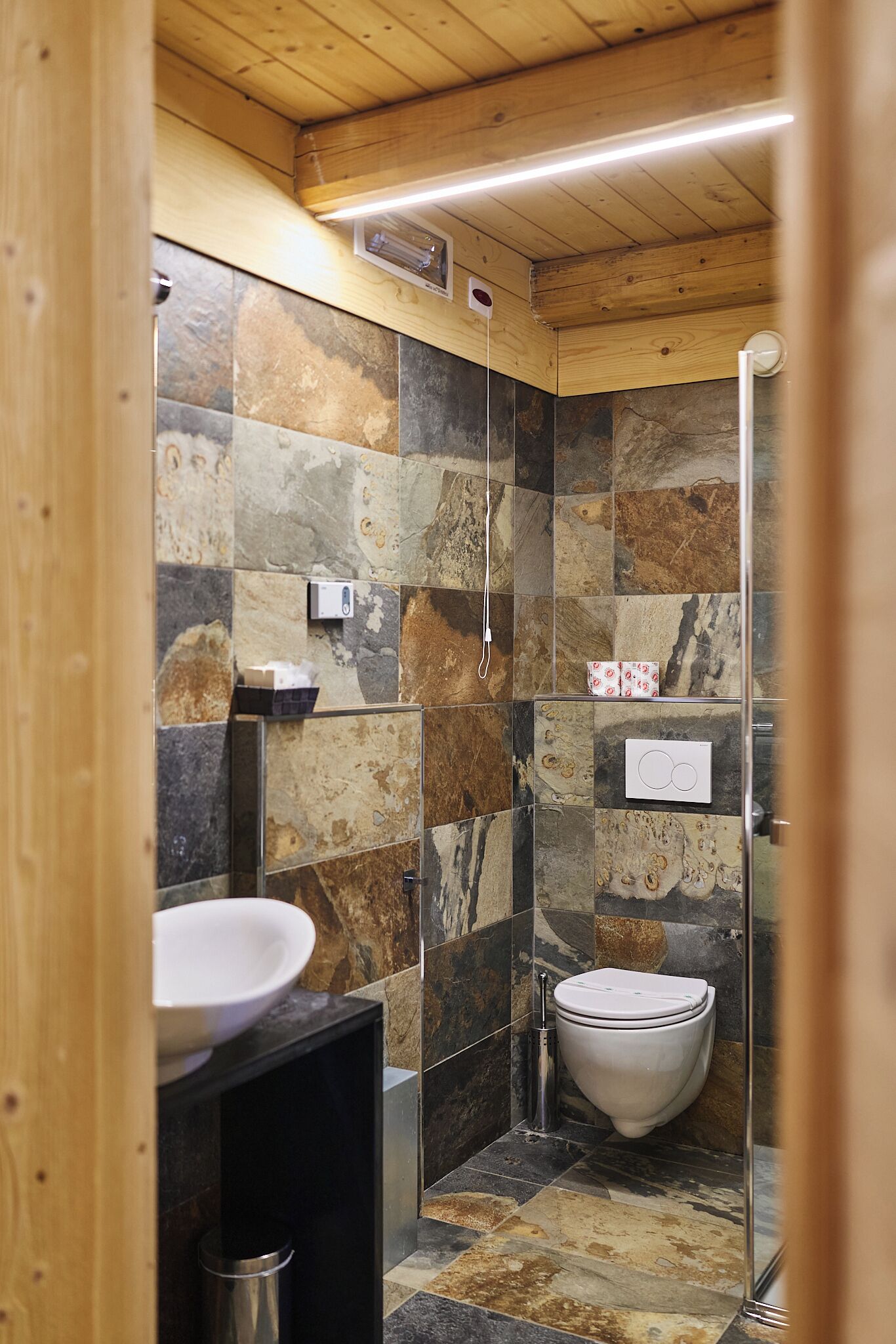 A bathroom with a stone tile wall, a white sink, and a toilet.