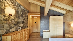 A wooden interior with a stone wall, wooden cabinets, and a bed. - Chalet Morel 1586 - Hotel & Spa (Limone Piemonte)