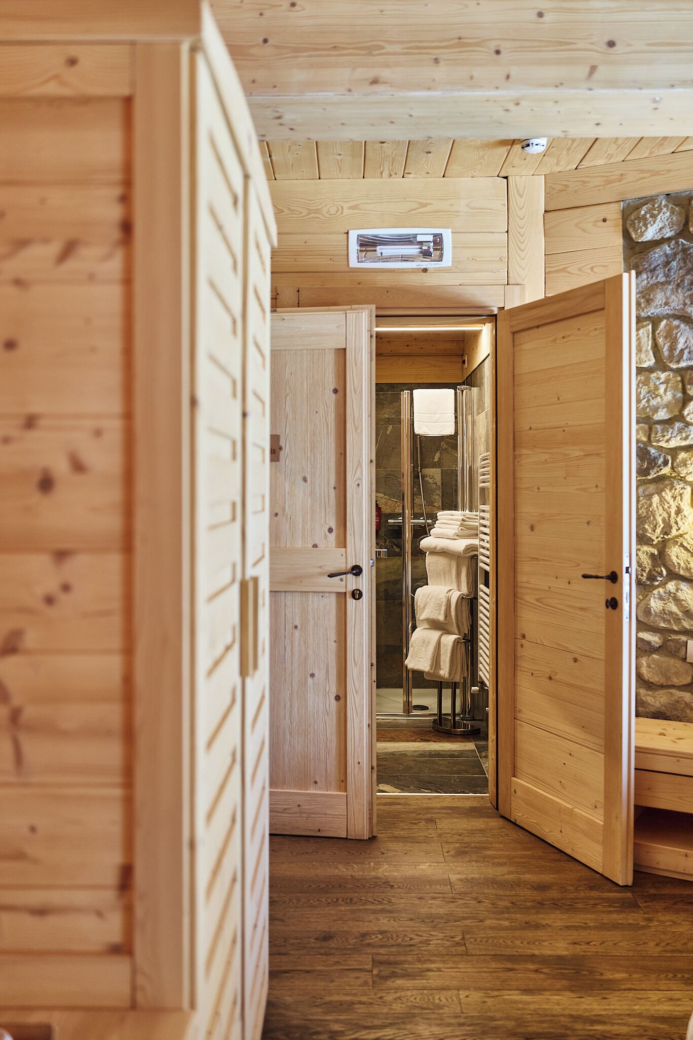 Ein Holzinnenraum mit einer Steinwand, einem Badezimmer mit Handtüchern und einem Holzboden.
