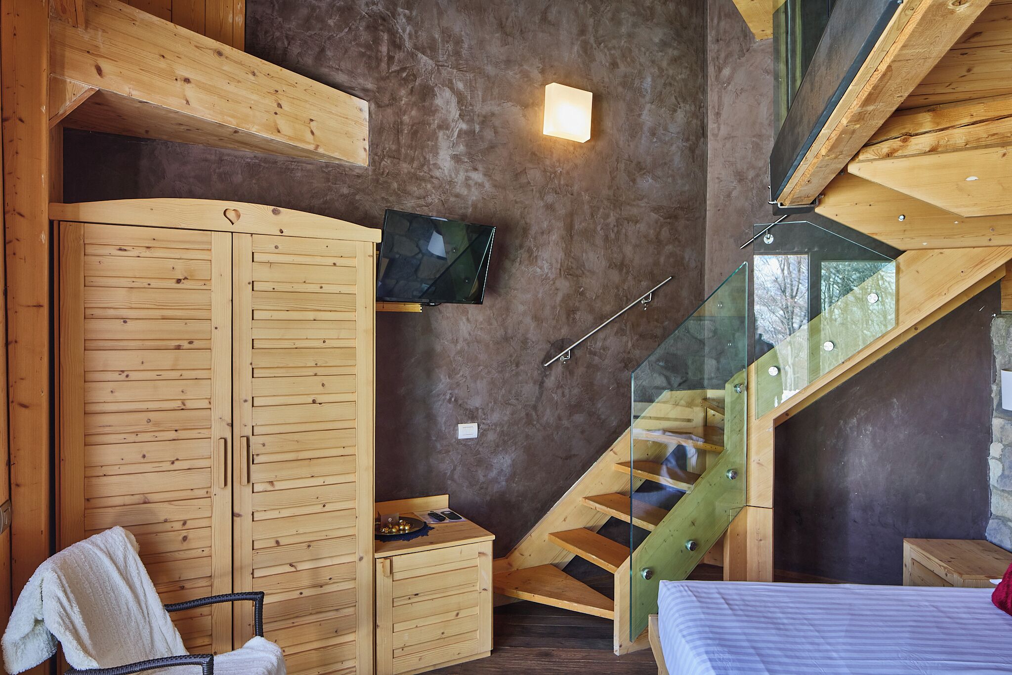 Ein Schlafzimmer mit Holzschrank, Bett und kleinem Schreibtisch, sowie einer Treppe.