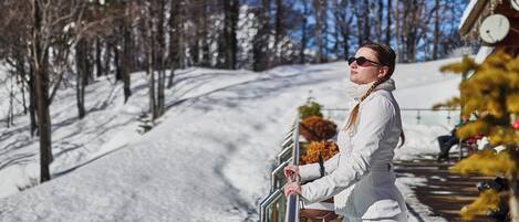 A person standing on a balcony with a snowy landscape and trees in the background.