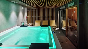 A modern spa area with a large heated pool, wooden slatted ceiling, and glass-enclosed seating areas. - Chalet Morel 1586 - Hotel & Spa (Limone Piemonte)