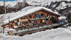 A wooden chalet with a glass bridge leading to a dining area, surrounded by snow-covered mountains. - Chalet Morel 1586 - Hotel & Spa (Limone Piemonte)