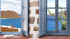 A room with a stone wall, a large window with multiple panes, and a view of a coastal landscape.
