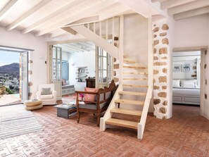 A spacious living area with a wooden staircase, a stone wall, and a view of the city.