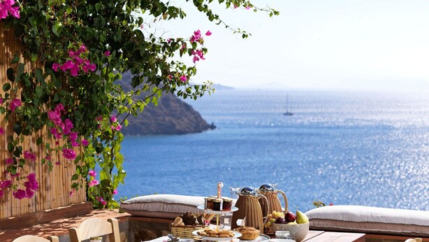 A table set for breakfast with a view of the sea and a mountain in the background.