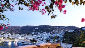 A wooden table with cushions and a lantern, overlooking a coastal town with white buildings and a body of water.