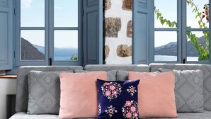 A room with a stone wall, a grey sofa with patterned cushions, and large windows with a view of a mountainous landscape.