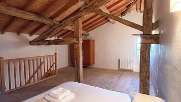 Une chambre avec un plafond en bois, un lit recouvert de draps blancs, une commode en bois et un radiateur.