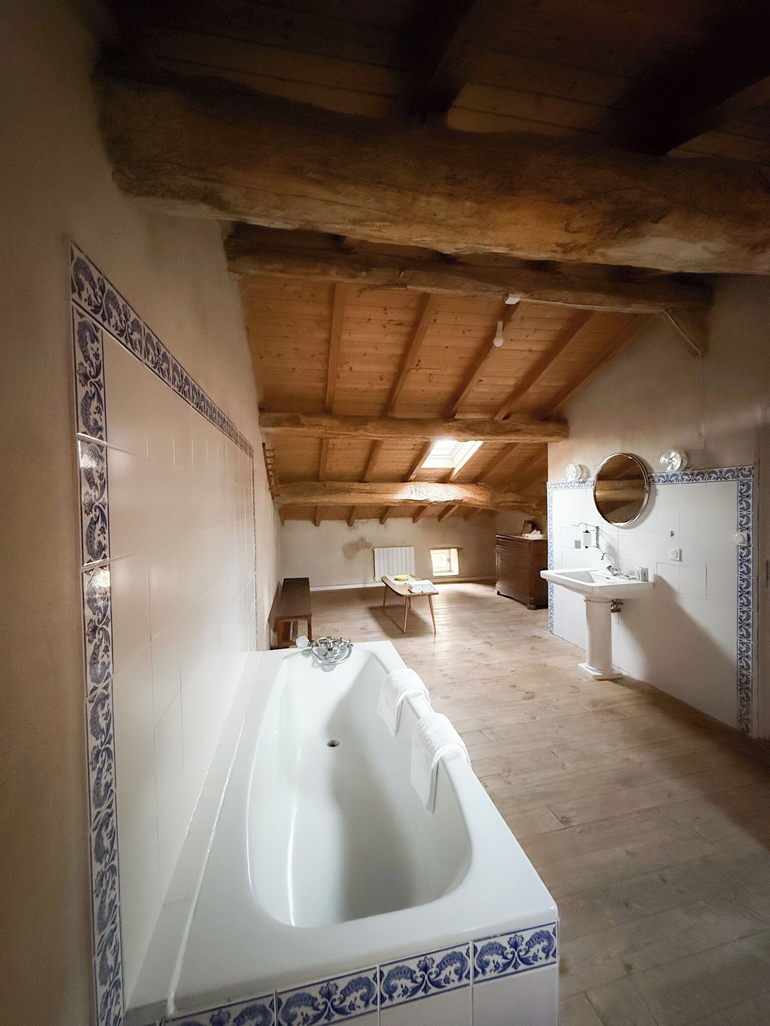 Un baño espacioso con una bañera grande, un lavabo y un espejo. La habitación tiene vigas de madera en el techo y paredes con baldosas.