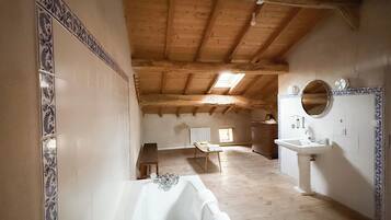 Un baño espacioso con una bañera grande, un lavabo y un espejo. La habitación tiene vigas de madera en el techo y paredes con baldosas.
