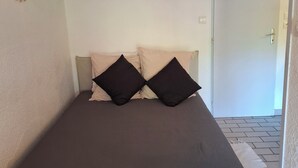 Een kleine, verzorgde slaapkamer met een bed, een zacht tapijt en een houten hoofdbord.