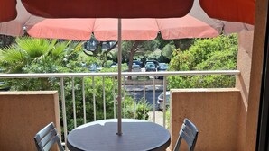 Een ronde tafel met vier stoelen onder een grote parasol op een balkon met uitzicht op geparkeerde auto's en groen.