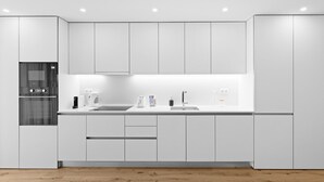 Una cocina moderna con armarios blancos, horno empotrado, pileta y cafetera.