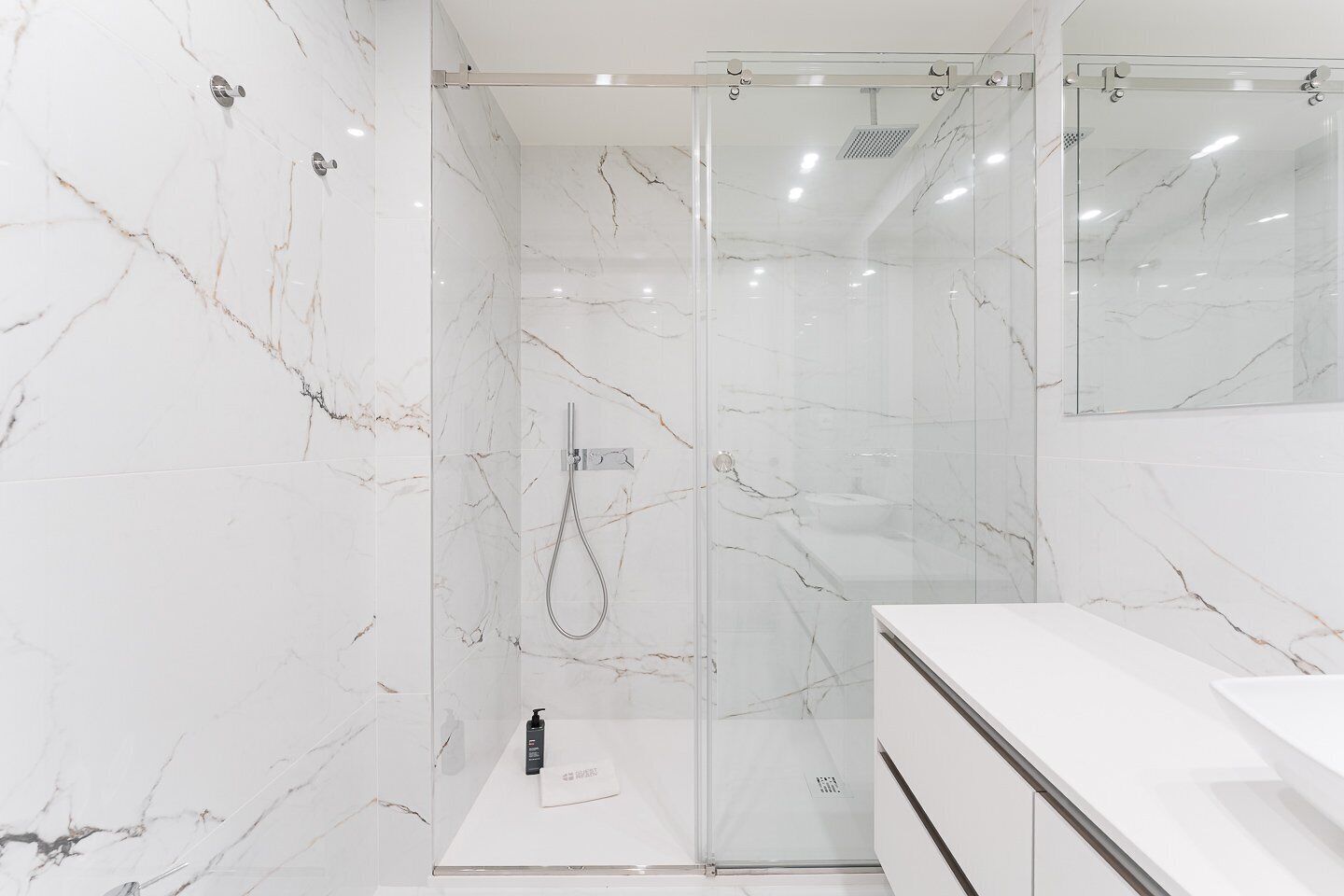 Une salle de bain moderne avec des murs en marbre, une douche en verre et un meuble-lavabo blanc.