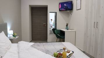 Ein Hotelzimmer mit Bett, Schreibtisch, Fernseher und einem Tablett mit Frühstücksangeboten.