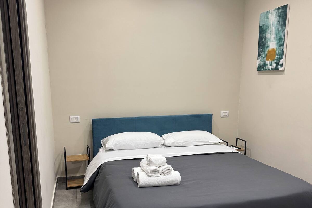 Una cama bien hecha con ropa de cama y toallas blancas, un cabecero azul y un suelo gris.