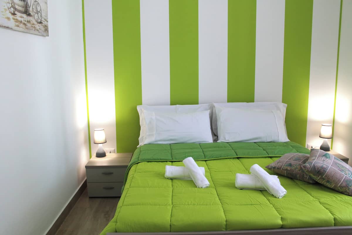 Una cama bien tendida con ropa de cama verde, dos almohadas y toallas enrolladas.
