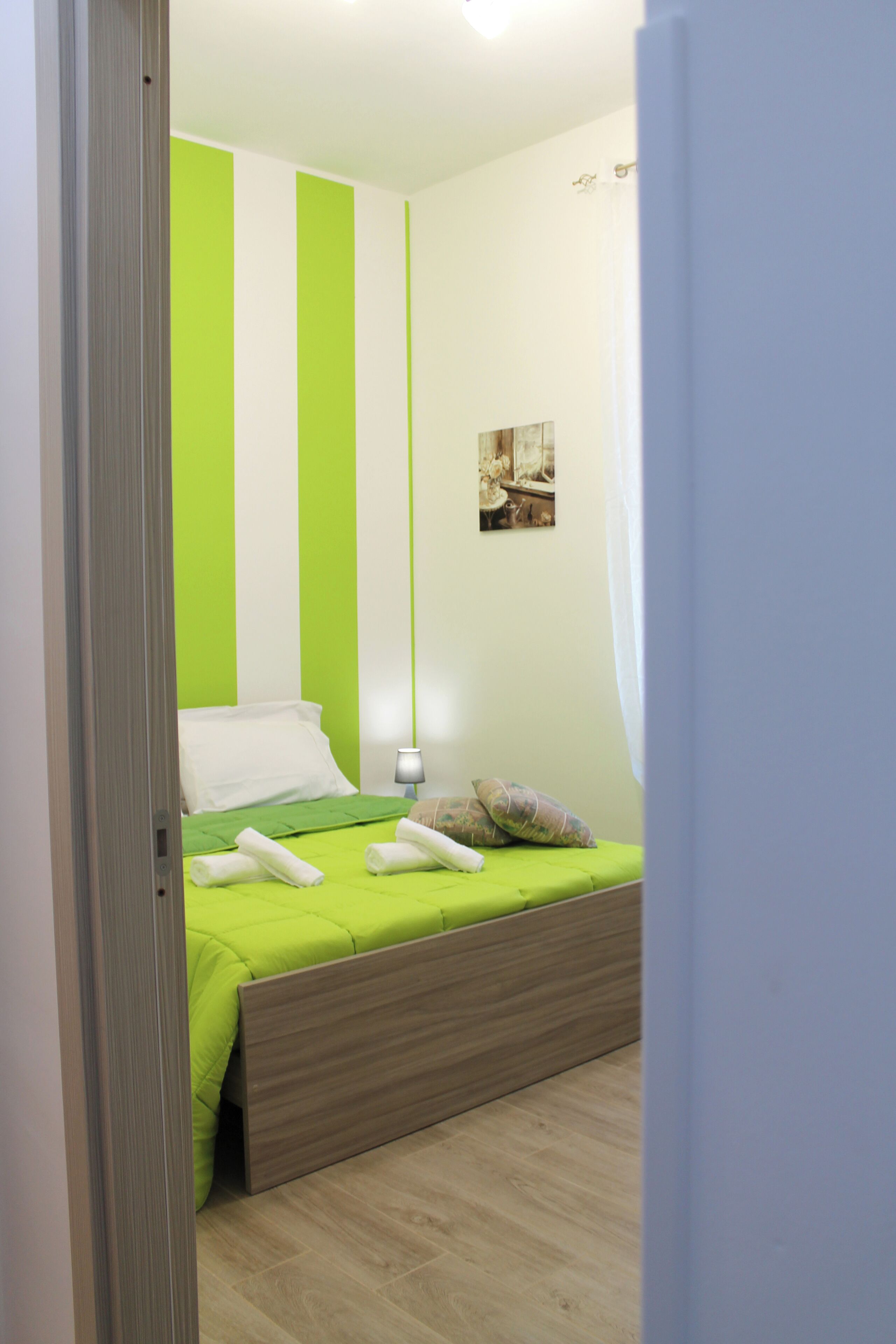 A bedroom with a bed, green and white striped walls, a wooden headboard, a bedside lamp, and a small picture on the wall.