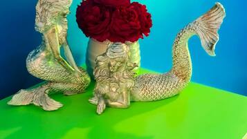 A mermaid figurine and a vase with red flowers on a green surface against a blue background.