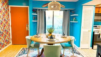 A dining area with a round table, four chairs, a chandelier, and a patterned rug.