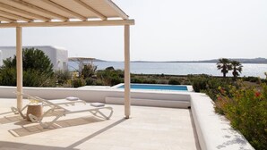 Un espace aménagé au bord de la piscine, avec une pergola, des chaises longues et une vue sur la mer.