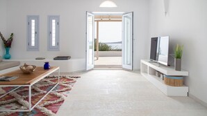 Un salon moderne avec un canapé, une table basse, un téléviseur posé sur un meuble et une vue sur un balcon extérieur, accessible par une porte ouverte.