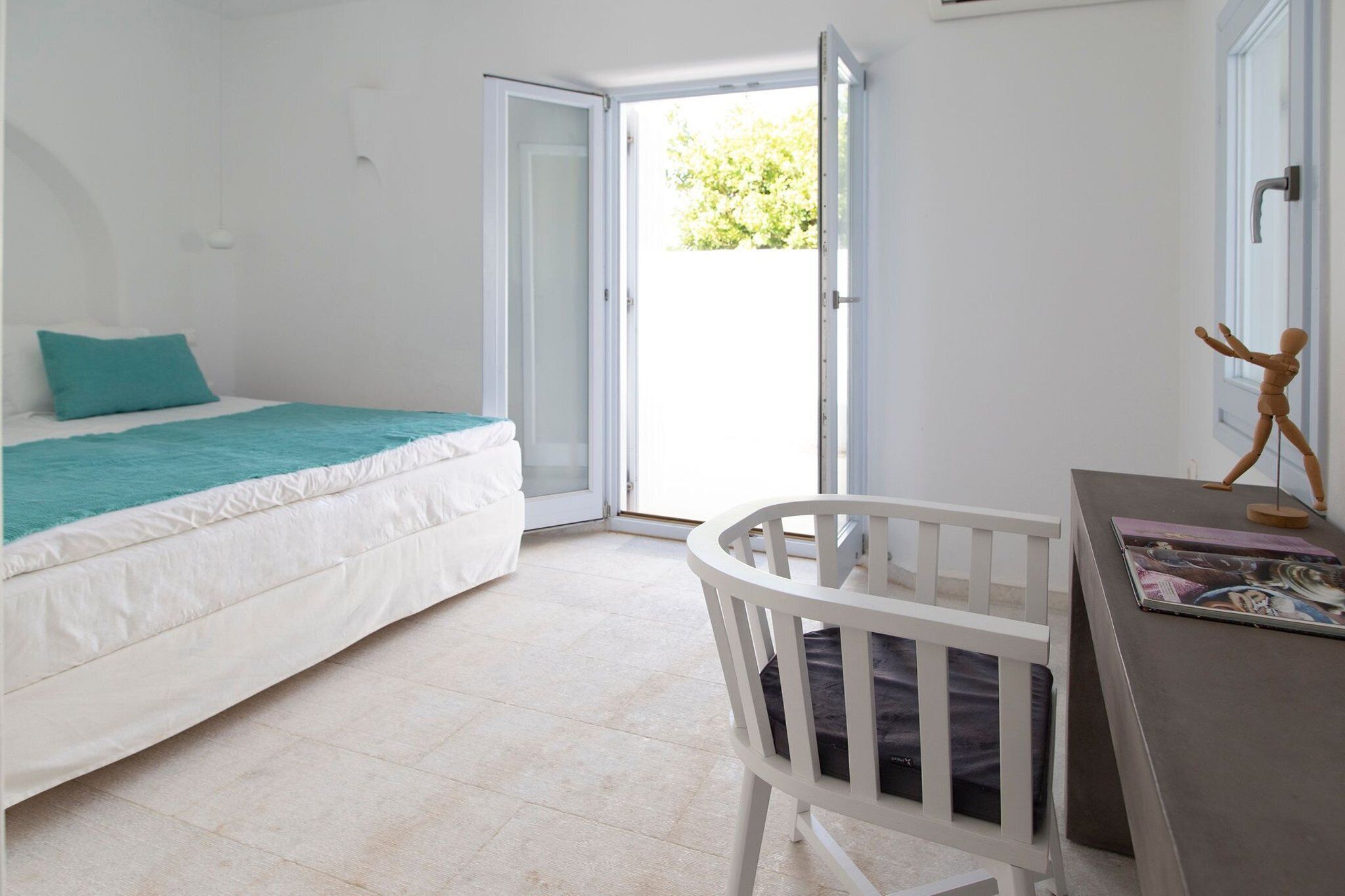 Quarto com cama, berço, mesa com revistas e porta para área externa.