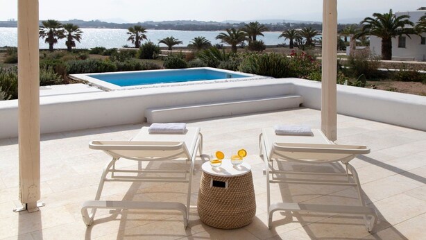 Un espace aménagé au bord de la piscine, comprenant deux chaises longues, une petite table ronde avec une bouteille et un verre, et offrant une vue sur la mer et les montagnes.