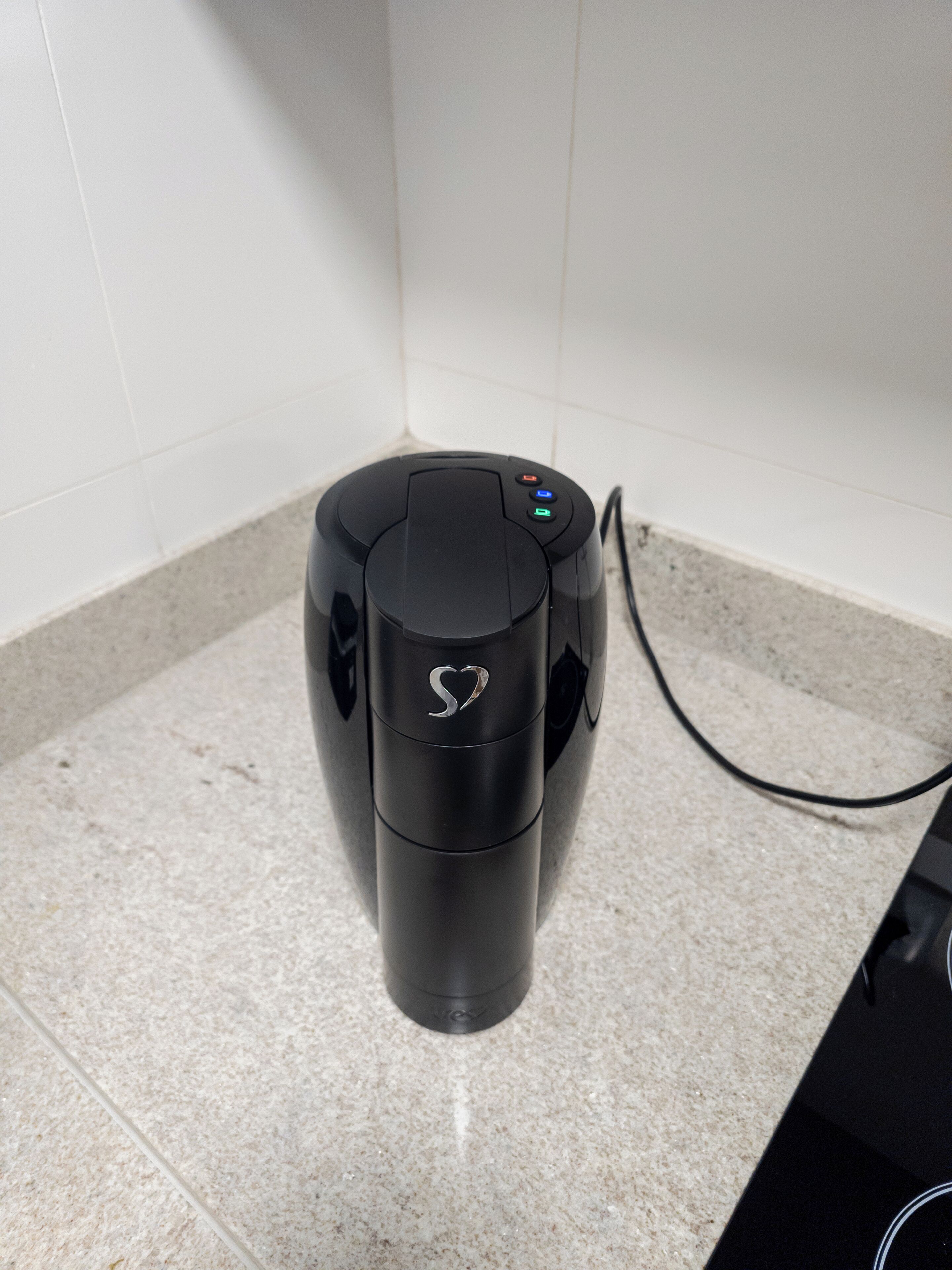 A black coffee maker with a heart-shaped logo on the top, connected to a power outlet.