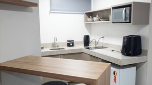 Une cuisine compacte avec une table en bois, un tabouret noir, un four à micro-ondes, une machine à café et un petit réfrigérateur.