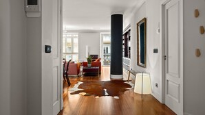 A hallway with a wooden floor, a large black column, and a red sofa in the background. - Versailles | The Rentals Collection (San Sebastián/Donostia)