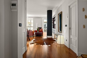 A hallway with a wooden floor, a large black column, and a red sofa in the background. - Versailles | The Rentals Collection (San Sebastián/Donostia)