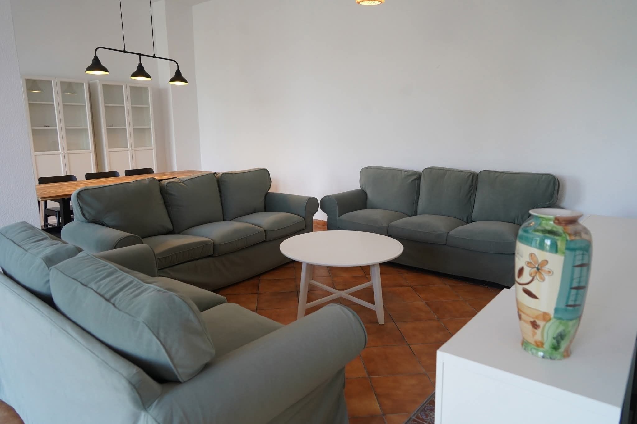 A modern living room with a sectional sofa, a small white table, and a dining area with chairs and a table.