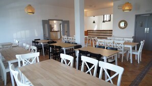A spacious dining area with multiple tables and chairs, a kitchen in the background, and pendant lighting. - Hotel Rural Mirador de Jubrique (Jubrique)