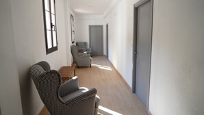 A hallway with a checkered armchair, a grey armchair, and a wooden table. - Hotel Rural Mirador de Jubrique (Jubrique)
