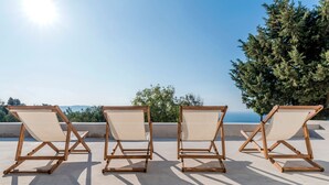 Three wooden lounge chairs with canvas seats on a rooftop terrace, overlooking a body of water and a forested area. - Alluring Mykonos Villa | Villa Kyma | 4 Bedrooms | Panoramic Sea Views |. (Mykonos)
