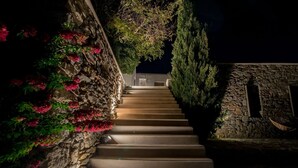 A stone staircase with steps leading up to a building, surrounded by greenery and flowers. - Alluring Mykonos Villa | Villa Kyma | 4 Bedrooms | Panoramic Sea Views |. (Mykonos)