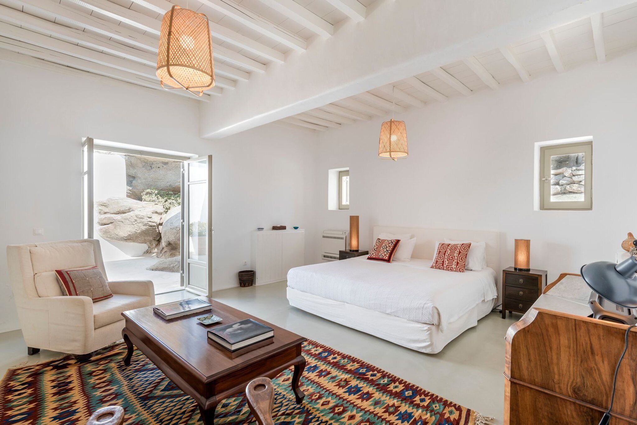 A spacious bedroom with a large bed, a sitting area with a chair and table, and a view of the outdoors.