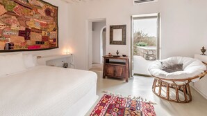 A bedroom with a large bed, a rattan chair, a patterned rug, and a wall tapestry. - Alluring Mykonos Villa | Villa Kyma | 4 Bedrooms | Panoramic Sea Views |. (Mykonos)