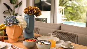 Een eettafel met een vaas, schalen met eten en een glas sap.