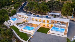 Een moderne villa met meerdere zwembaden, een ruim buitengebied en uitzicht op het omliggende landschap.