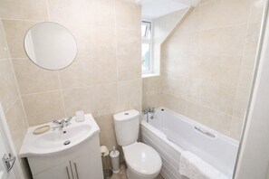 A bathroom with a sink, toilet, and bathtub, all in white, with beige tiles on the walls.