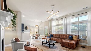 Un salon spacieux avec un canapé d’angle, un coin repas et de grandes fenêtres.